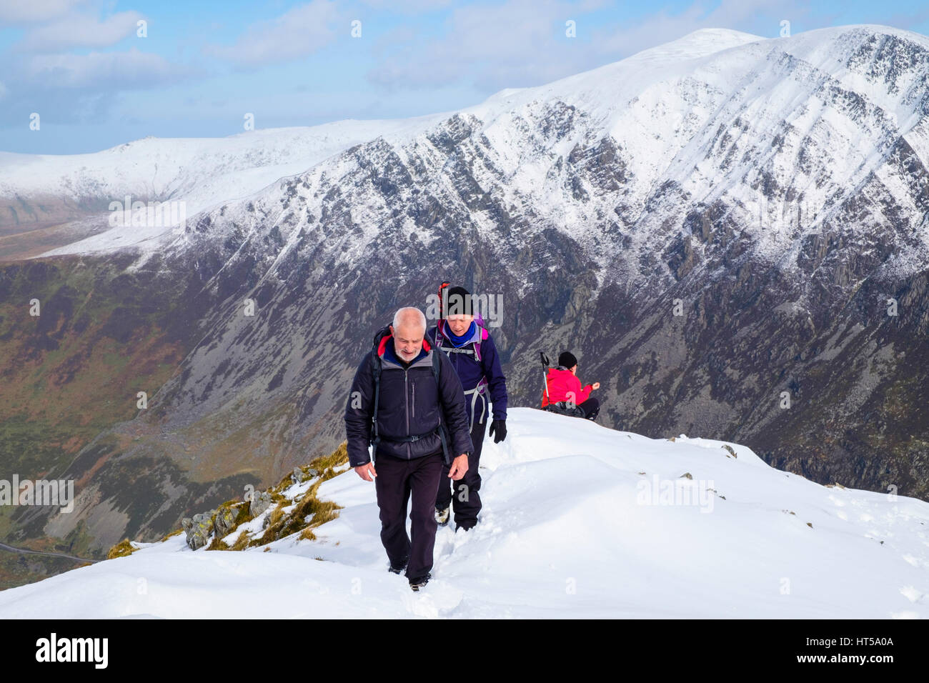 Two hikers hiking in snow on Y Garn north east ridge with view to Carneddau in Snowdonia National Park (Eryri) mountains. Ogwen Gwynedd North Wales UK Stock Photo