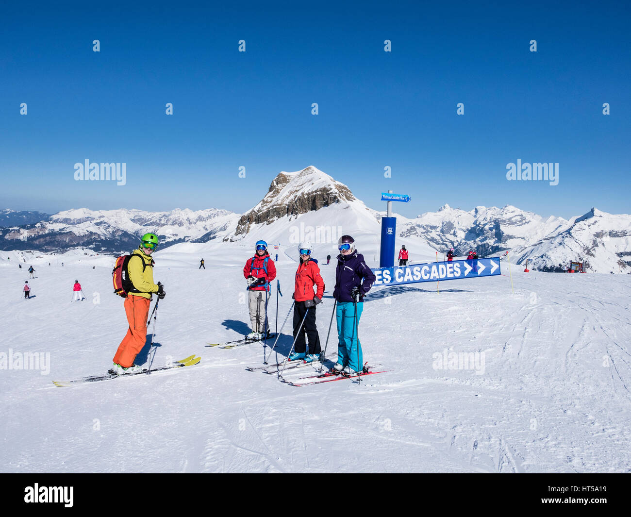 Four skiers by Piste des Cascades sign whilst skiing on snow slopes high in mountains of French Alps. Flaine, Haute Savoie, Rhone-Alpes, France Stock Photo