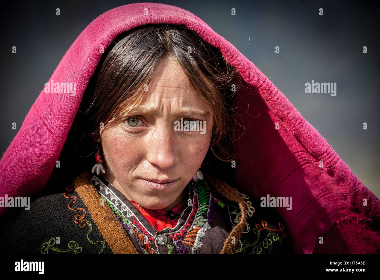 Afghanistan, Wakhan corridor, a portrait of Afghan woman with red veil and blue eyes. Stock Photo