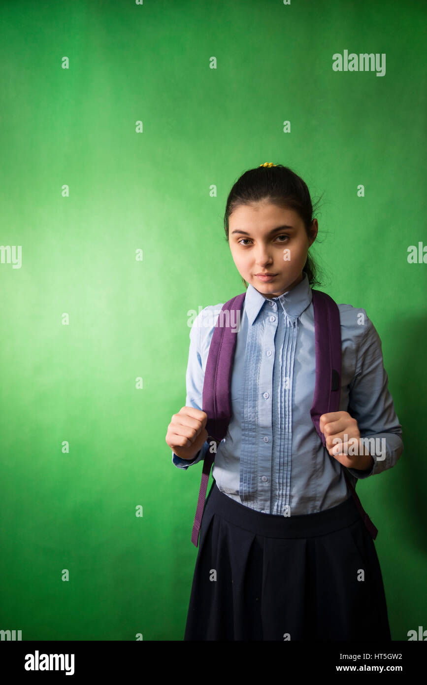 one teen schoolgirl in blue shirt is standing with a purple backpack on his shoulders on a green  chroma key background Stock Photo