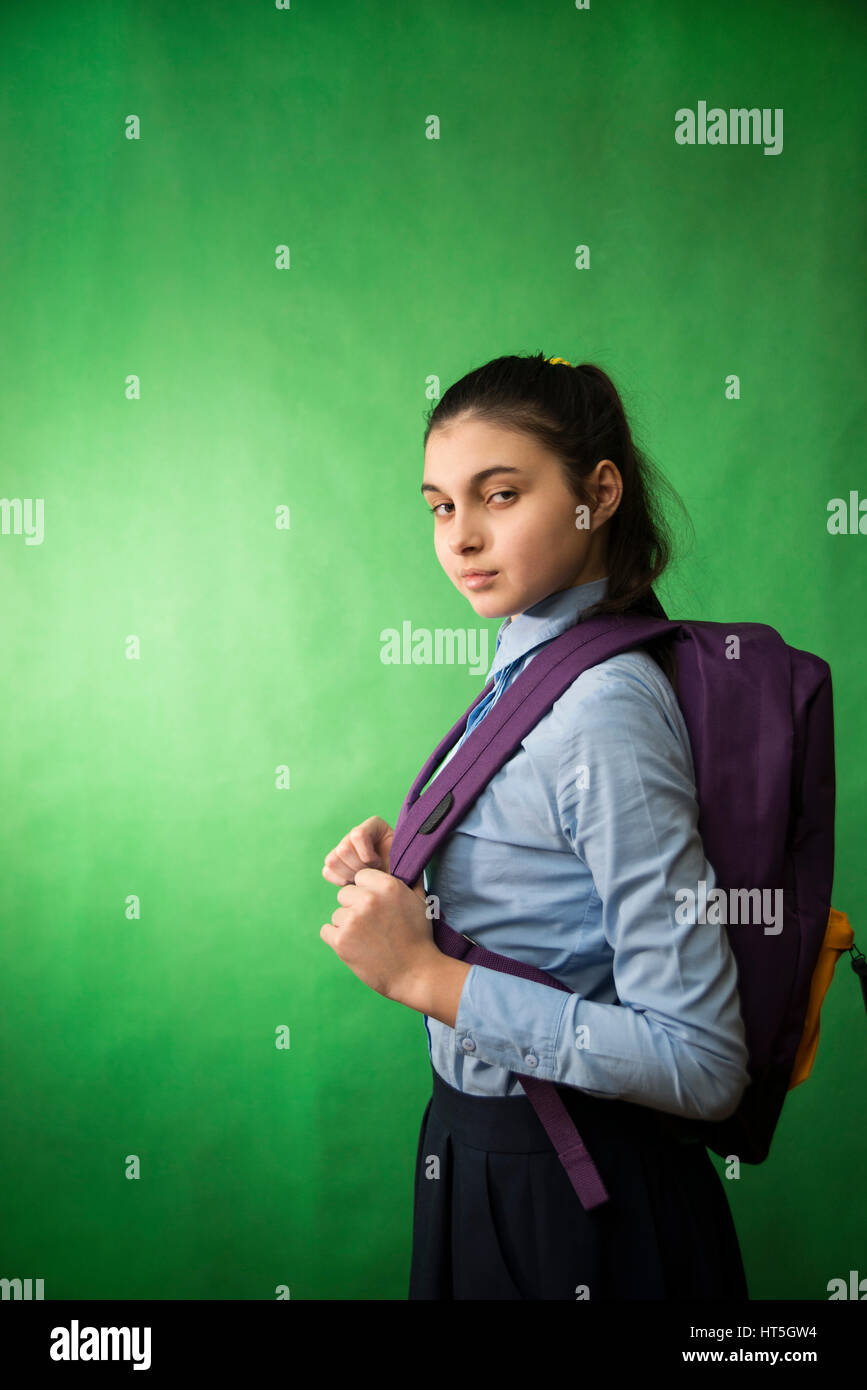 one teen schoolgirl in blue shirt is standing with a purple backpack on his shoulders on a green  chroma key background Stock Photo
