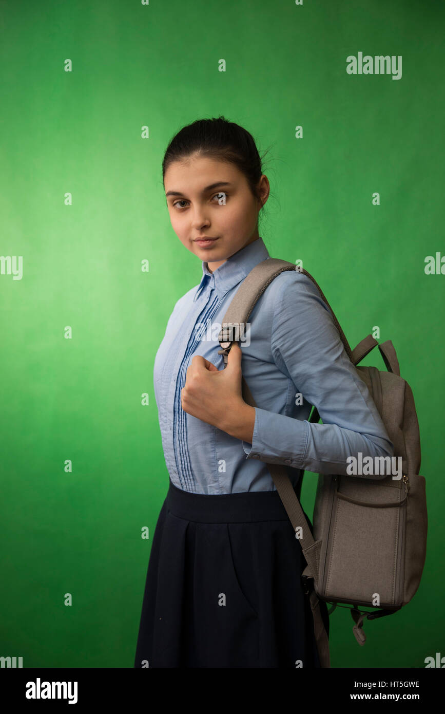 one teen schoolgirl in blue shirt  is standing with a grey backpack on his shoulders on a green chroma key background Stock Photo