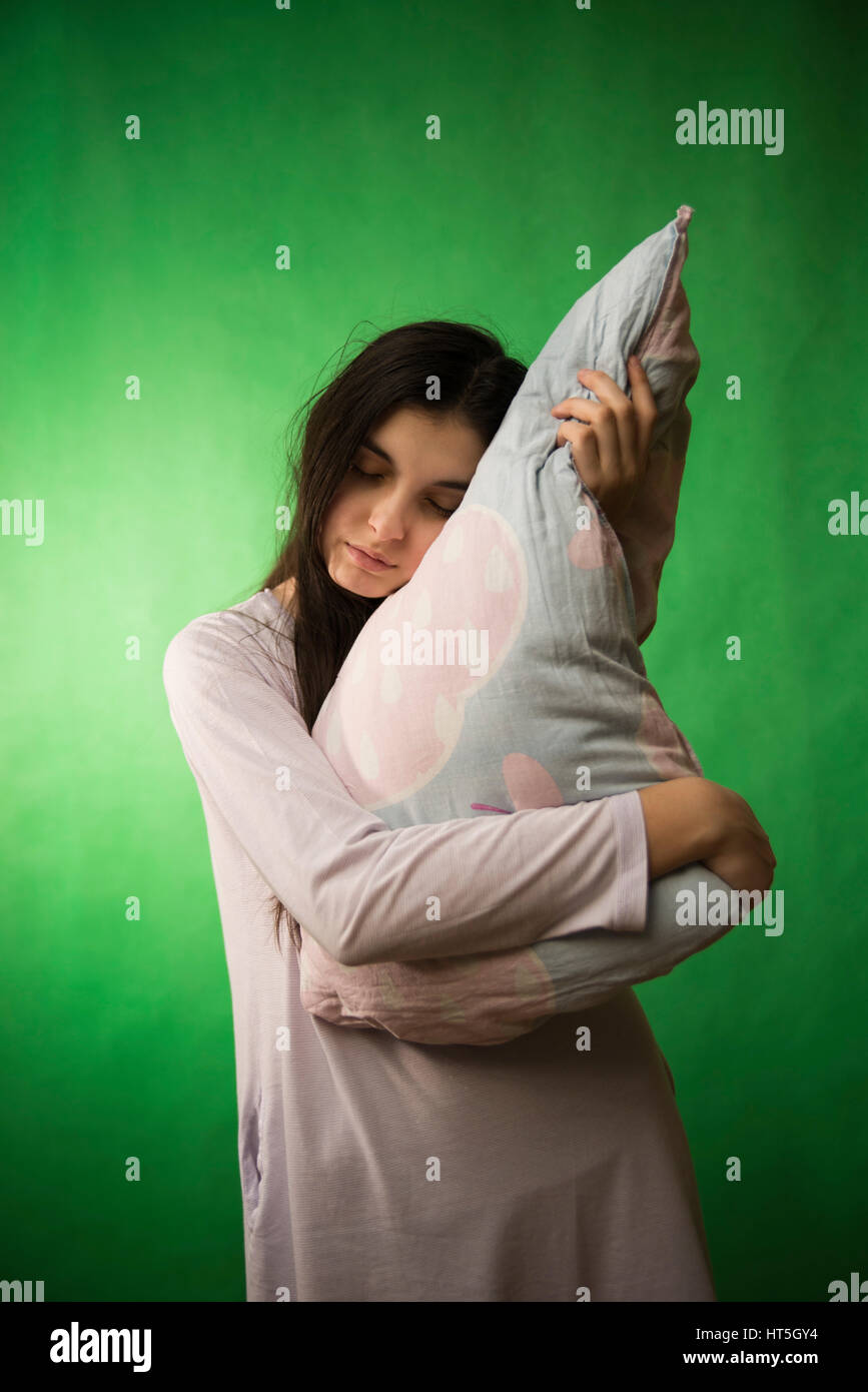 a girl in a nightgown leaned against the pillow on a green chroma key background Stock Photo