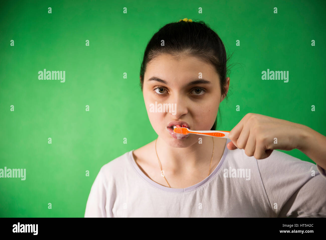 teen girl brushing her teeth with a toothbrush in nightie on a green chroma key background Stock Photo