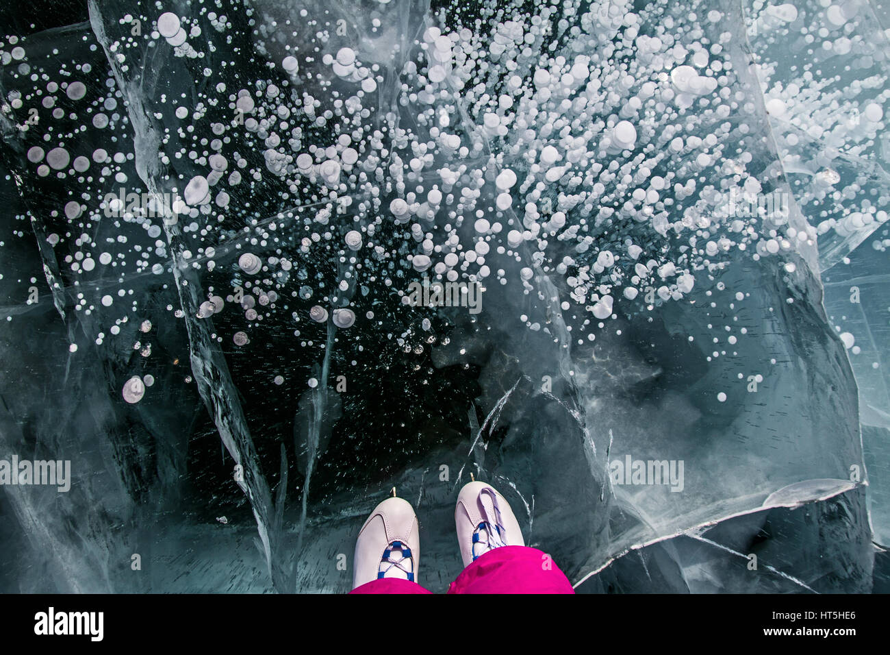 Skater in the pink pants on beautiful fairytale ice of the lake Baikal and cracks on ice and bubbles in ice. Stock Photo