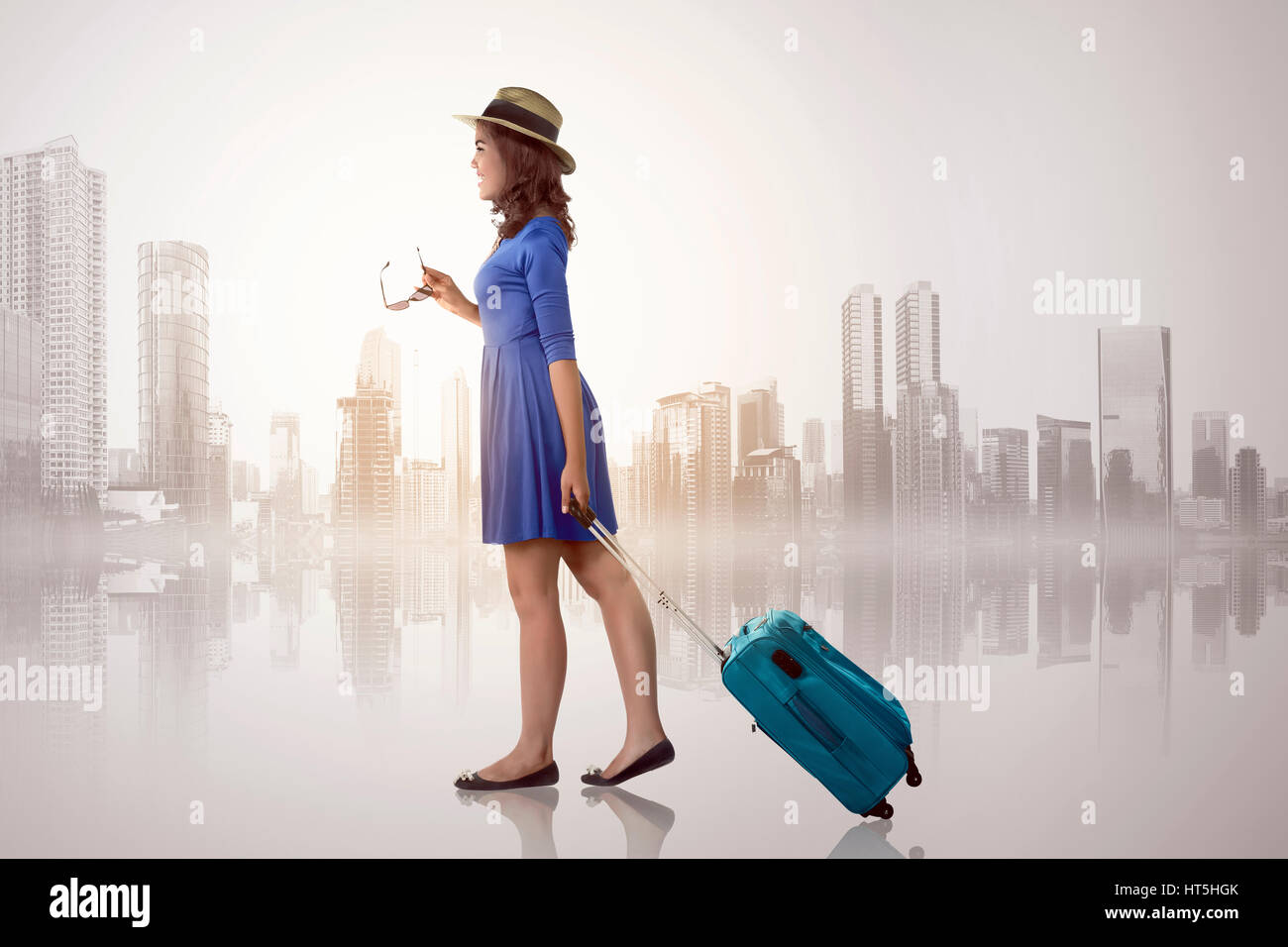 Young asian woman with hat holding suitcase over cityscape background Stock Photo