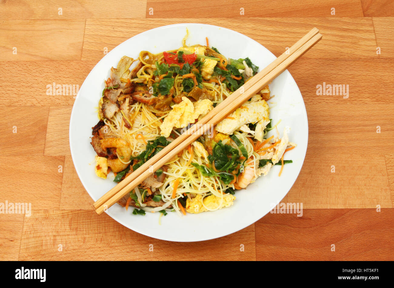 Singapore noodles in a bowl with chopsticks on a wooden tabletop Stock