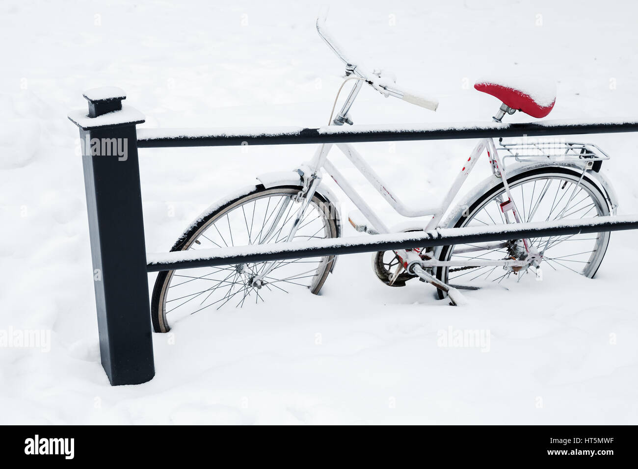 White bicycle parked near urban railings in snowdrift. European winter Stock Photo