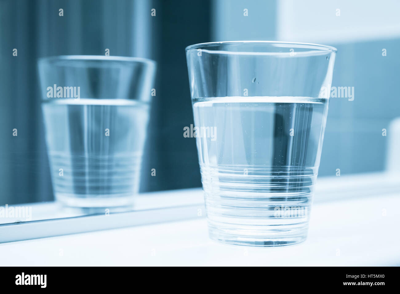 Glass of water stand on shelf near mirror, blue toned closeup photo Stock Photo