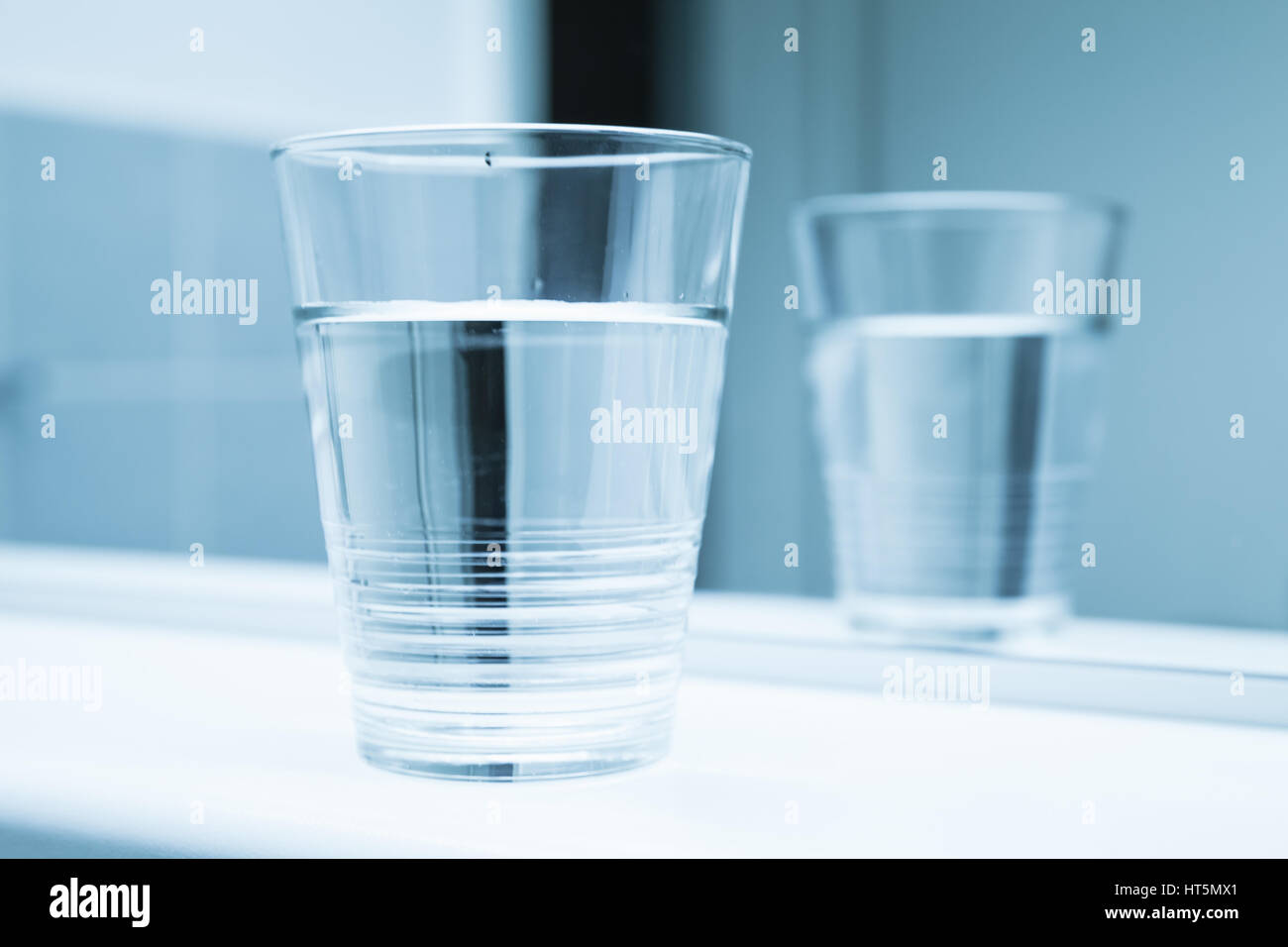 Glass of water stand on shelf near mirror, blue toned close-up photo ...