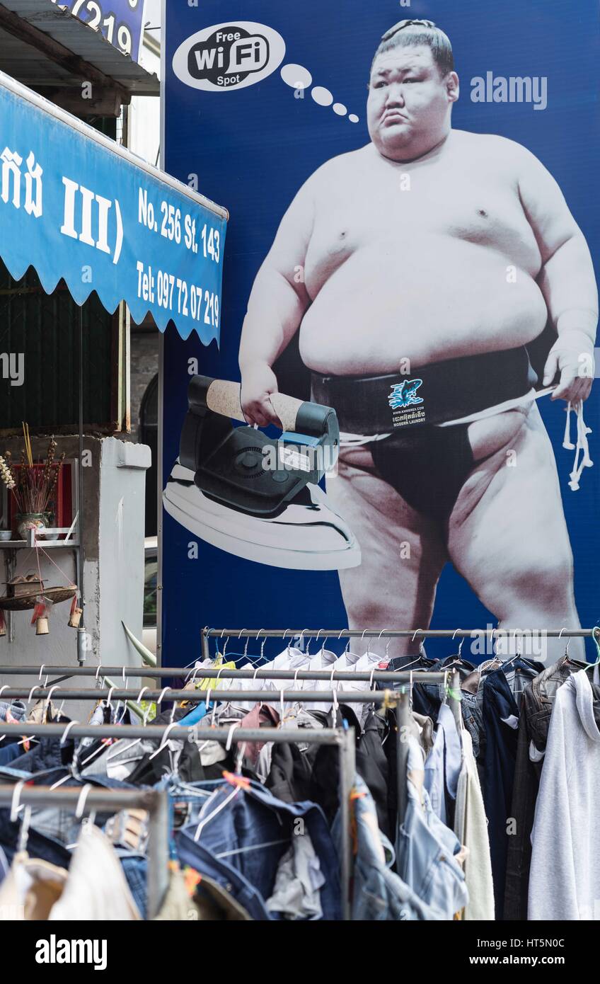 Sumo wrestler holding a large domestic iron.  Advertising board outside a laundry/ironing service. Cambodia Stock Photo