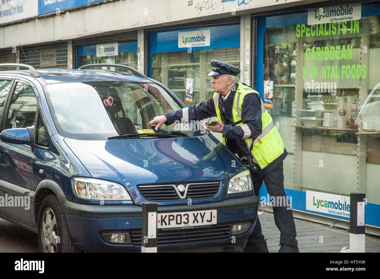 London, UK, 07/03/2017, Traffic warden attaching a parking ticket to a car at Brixton market. Stock Photo
