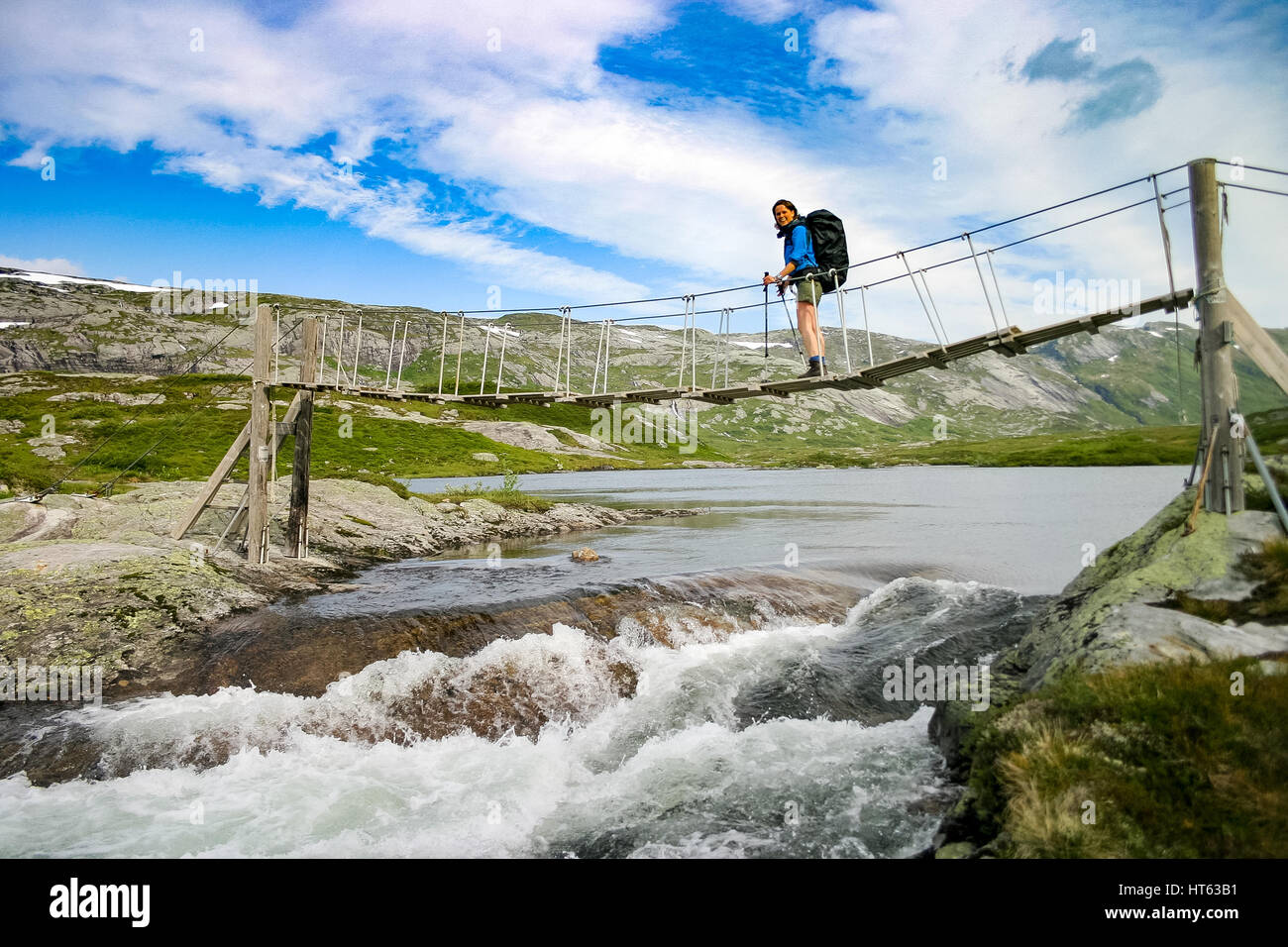 Young woman with backpack hiking across narrow wooden suspension bridge