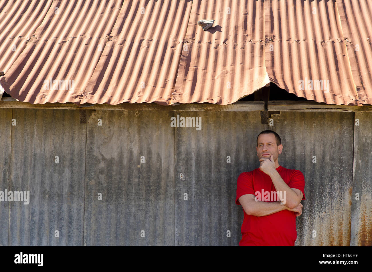 Man day dreaming with hand on his chin in front of a rural old building Stock Photo