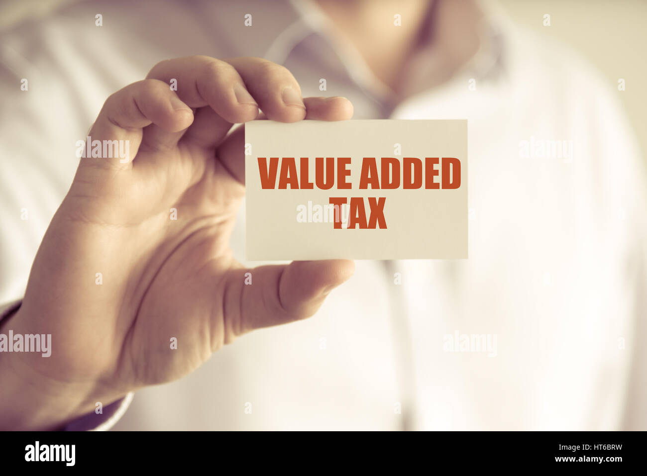 Closeup on businessman holding a card with text VALUE ADDED TAX, business concept image with soft focus background and vintage tone Stock Photo