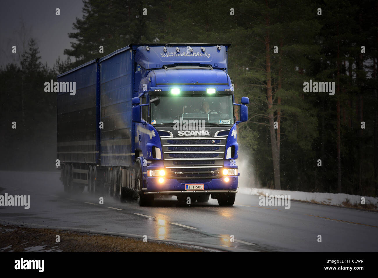 SALO, FINLAND - MARCH 4, 2017: Blue Scania R620 combination vehicle of M. Keskimaki transports goods along wet road in snowfall, high beams flashed br Stock Photo