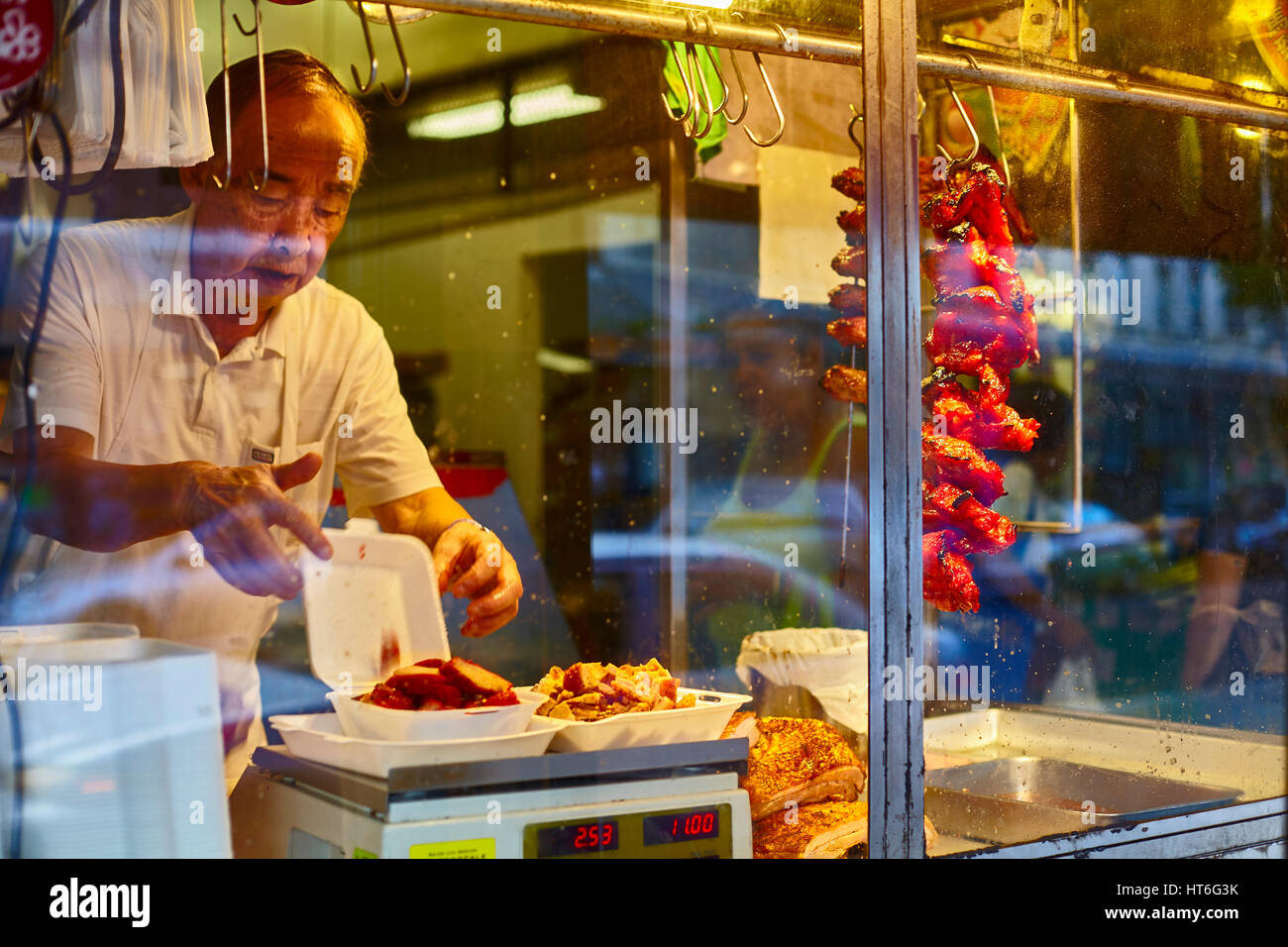 Honolulu; Hawaii; USA - August 6; 2016: A man prepares roast pork for a customer behind a glass wall at night in the Chinatown Historic District Stock Photo