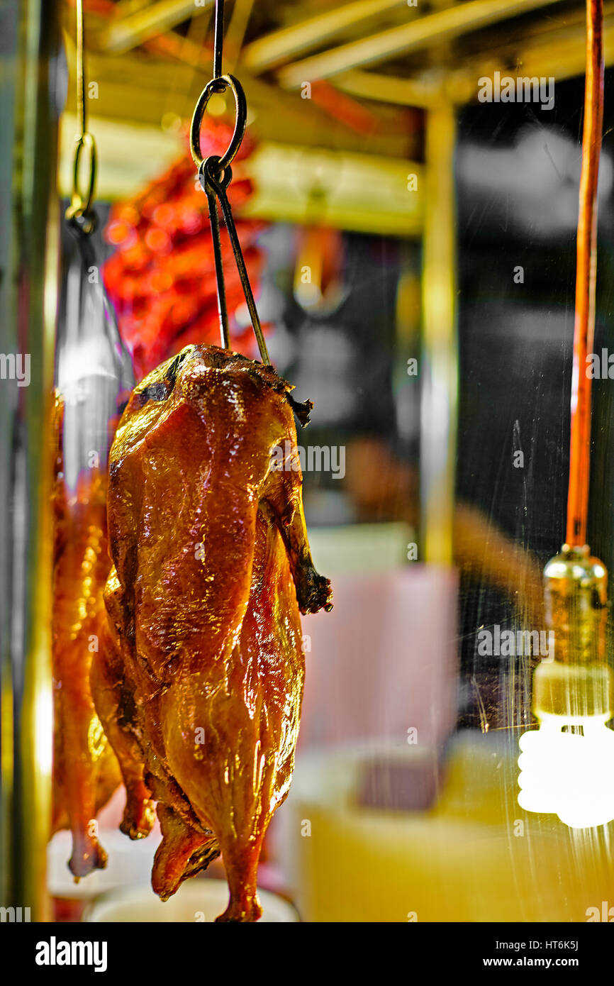 Chinese Roast Duck street food hanging on hook behind faded glass at night in downtown Chinatown Stock Photo