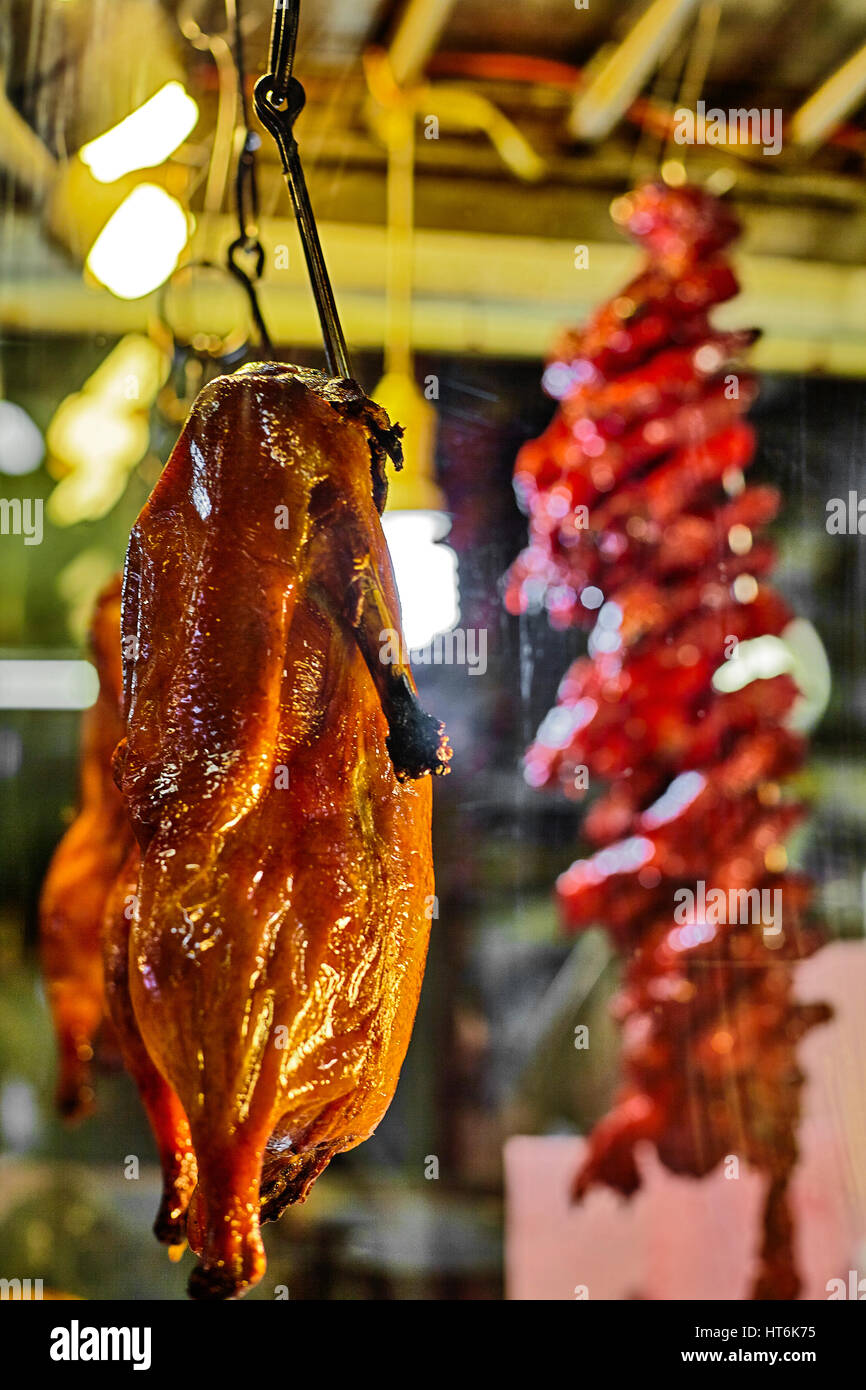Chinese Roast Duck hangs on a hook behind faded glass at a Chinatown market vendor at night closeup Stock Photo