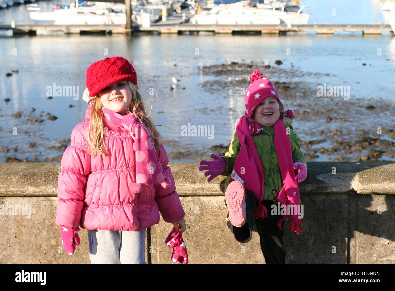 Two girls, children messing and dancing by the harbour wall on a cold windy day, Howth, Dublin Ireland Stock Photo