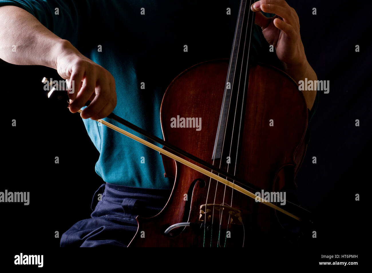 Man in blue shirt playing cello with a bow, his face hidden Stock Photo