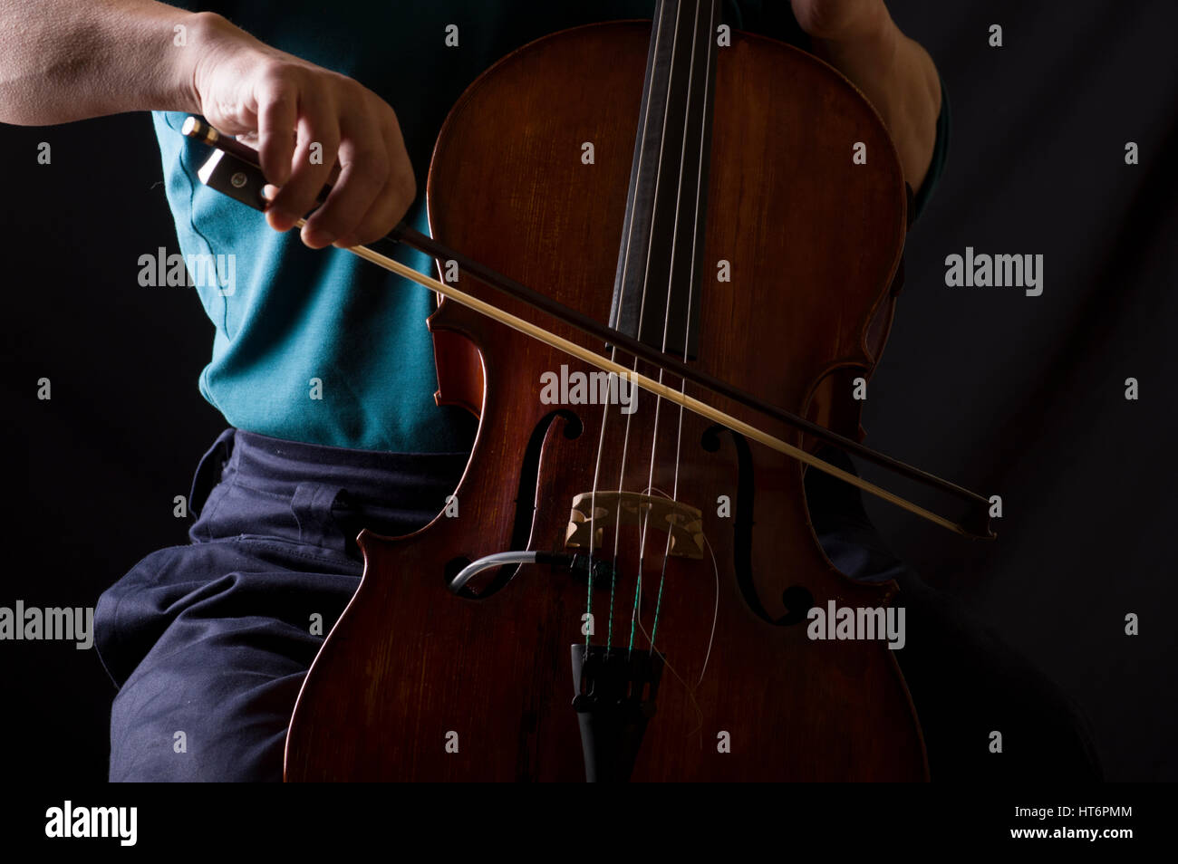 Man in blue shirt playing cello with a bow, his face hidden Stock Photo