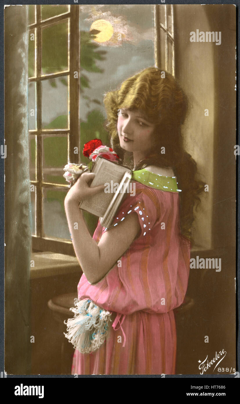 ITALY - CIRCA 1920: A postcard printed in Italy, shows a sad girl standing at the window with a book, circa 1920 Stock Photo