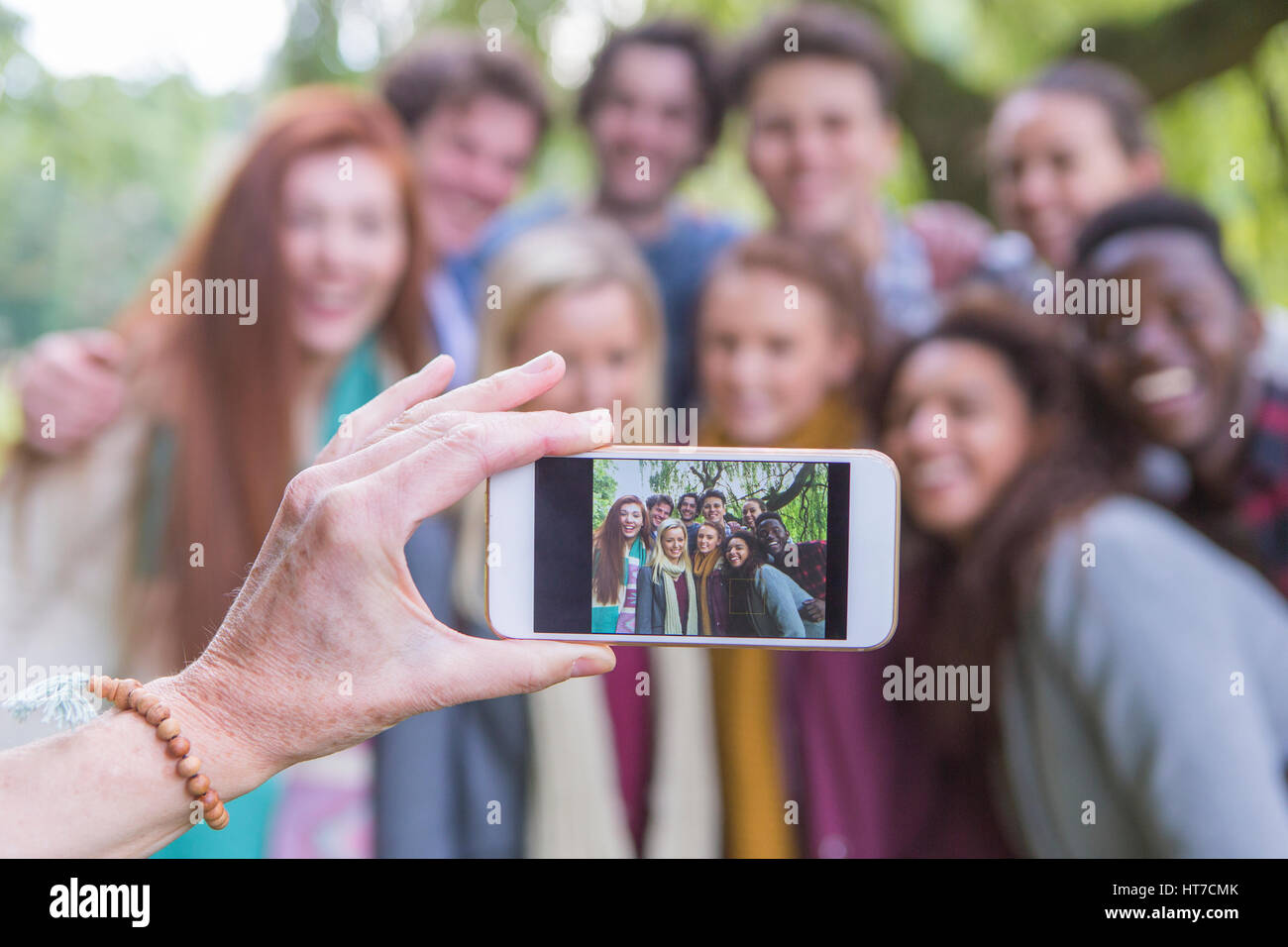 A happy group of students smile at the camera as someone takes an image of them on a mobile phone. The phone is being held by a mother taking an image Stock Photo
