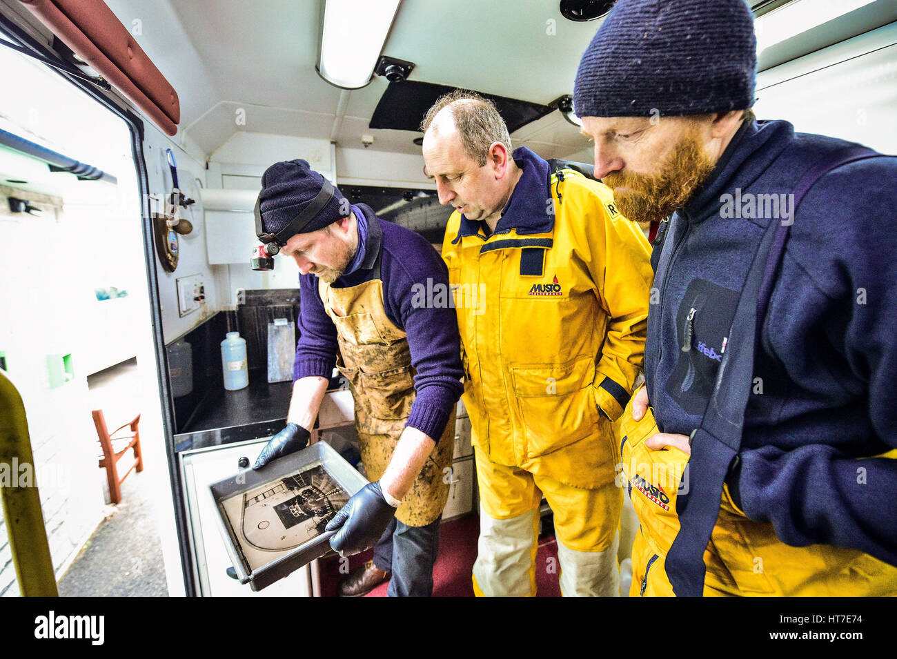 Photographer Jack Lowe, shows lifeboat crews a Victorian glass plate photograph he developed in his mobile darkroom, a decommissioned NHS ambulance, which he uses to travel with his Victorian glass plate camera in his mission to capture all 237 RNLI lifeboat stations in the UK and Ireland for the The Lifeboat Station Project. Stock Photo