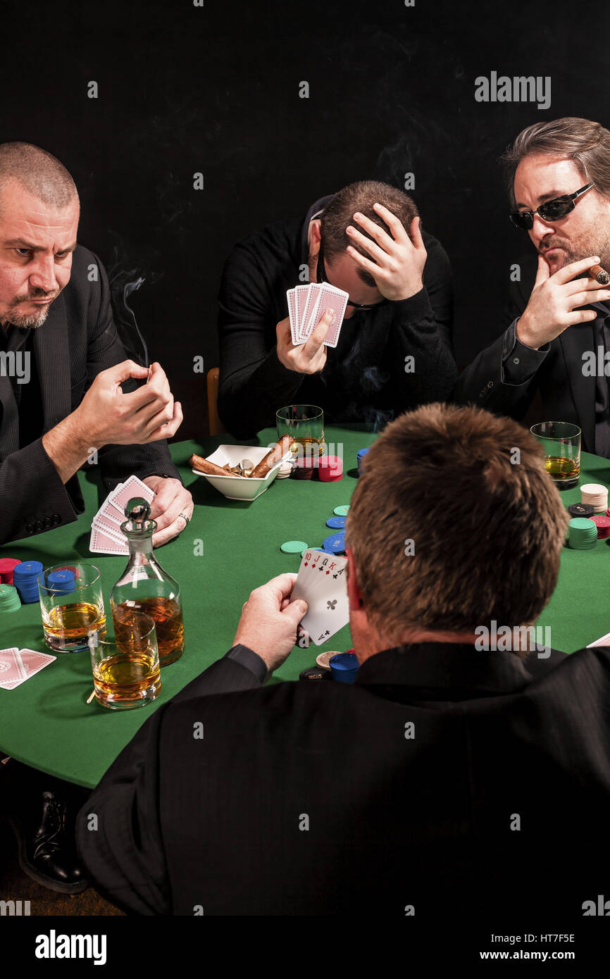 Photo of men playing poker, drinking and smoking, and looking uncertain of their luck. Stock Photo