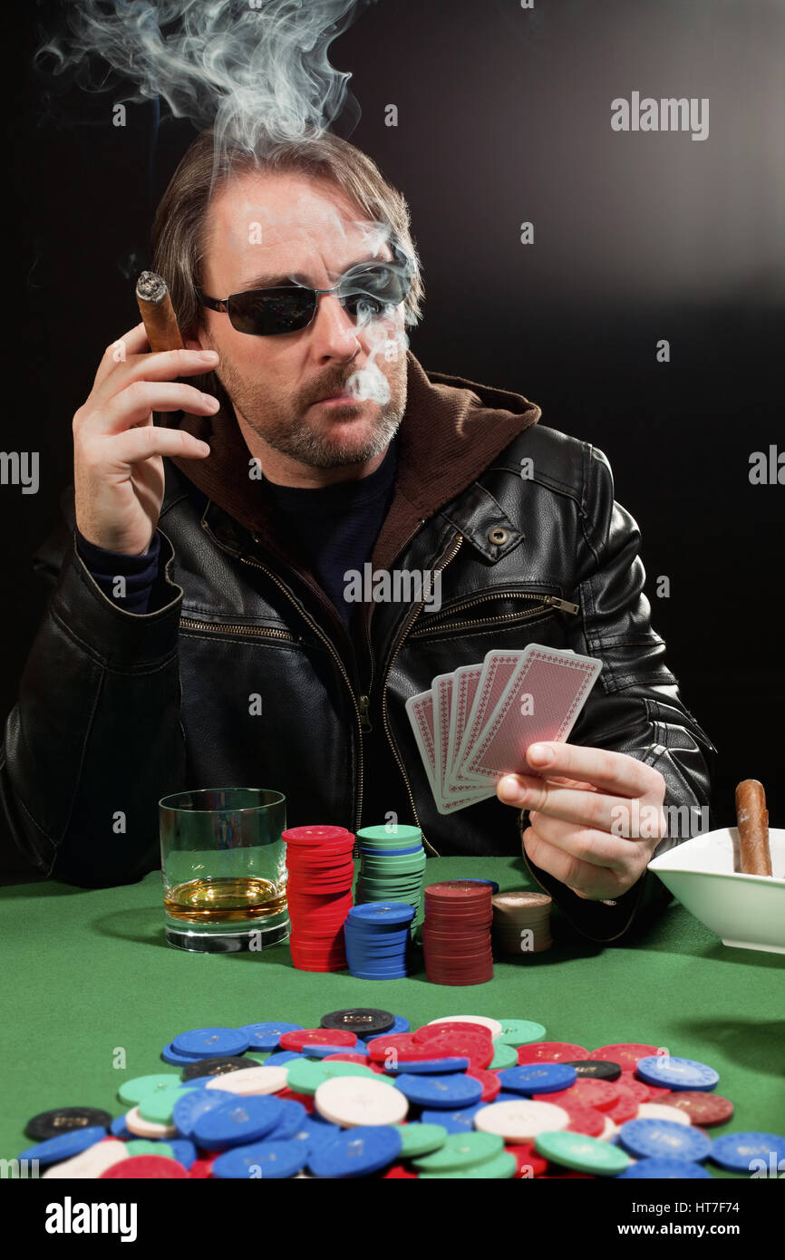 Photo of a man playing poker and smoking a cigar. Playing cards have