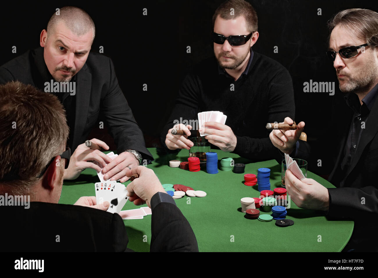 Photo of four men playing poker, smoking cigars and drinking whiskey. Focus is on the winning hand. Stock Photo