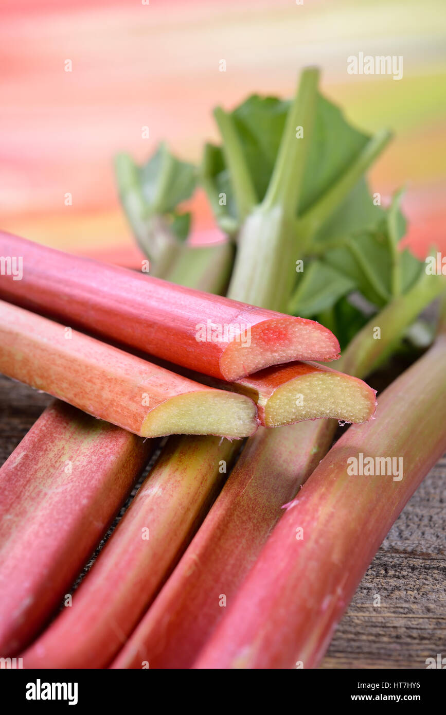 Fresh unpeeled rhubarb on a wooden table, in the background other rhubarb stalks in soft focus Stock Photo