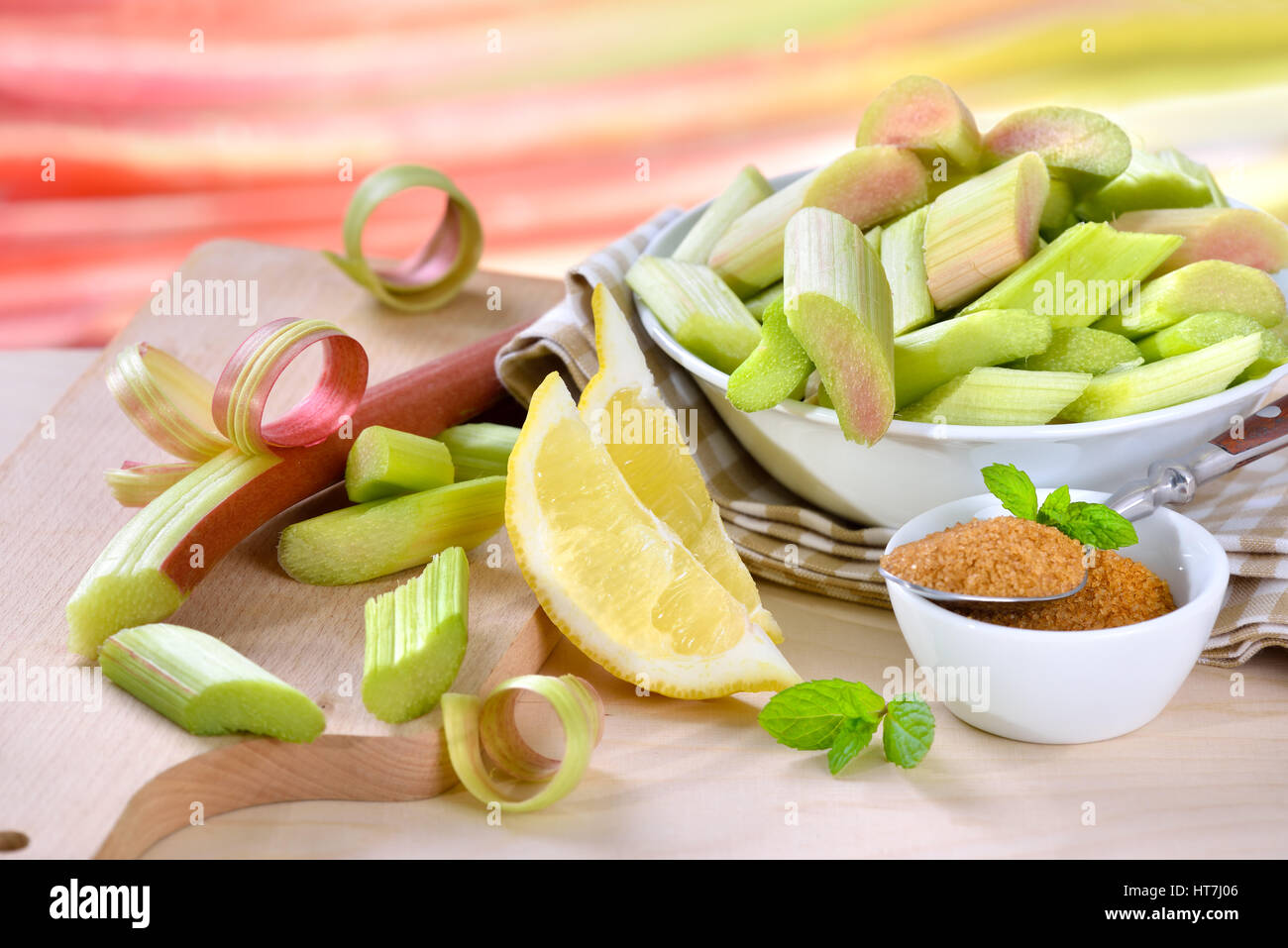 Peeled and chopped raw rhubarb prepared for cooking compote with brown sugar and lemon, in the background other rhubarb stalks in soft focus Stock Photo