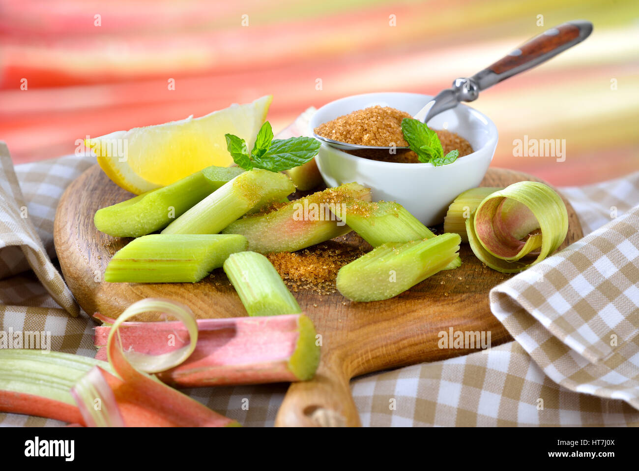 Peeled and chopped raw rhubarb prepared for cooking compote with brown sugar and lemon, in the background other rhubarb stalks in soft focus Stock Photo
