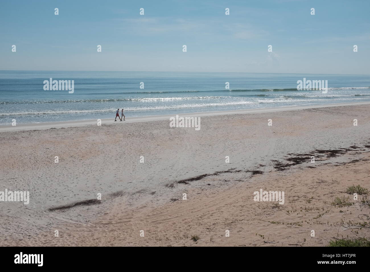 Far from crowds, a man and a woman take a stroll along beautiful Bethune Beach on a sunny day and under a blue sky while ocean waves gently roll in. Stock Photo