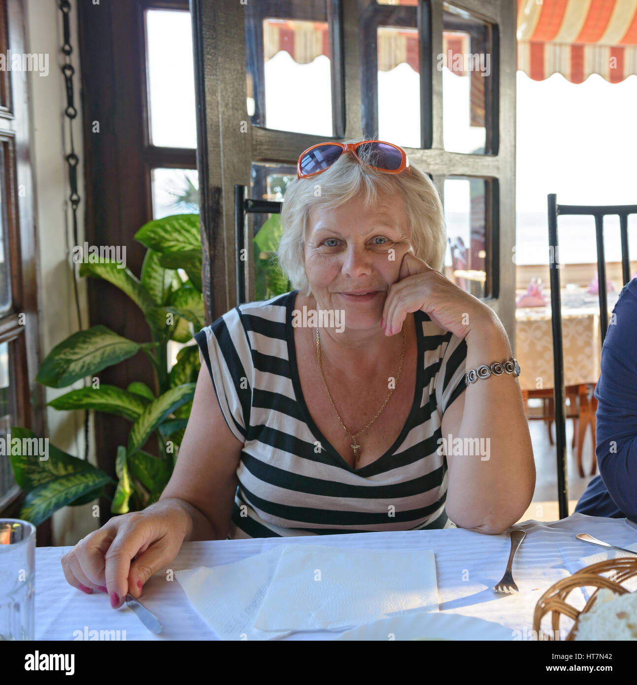 Aged woman is waiting for dinner dishes in resort cafe. Stock Photo