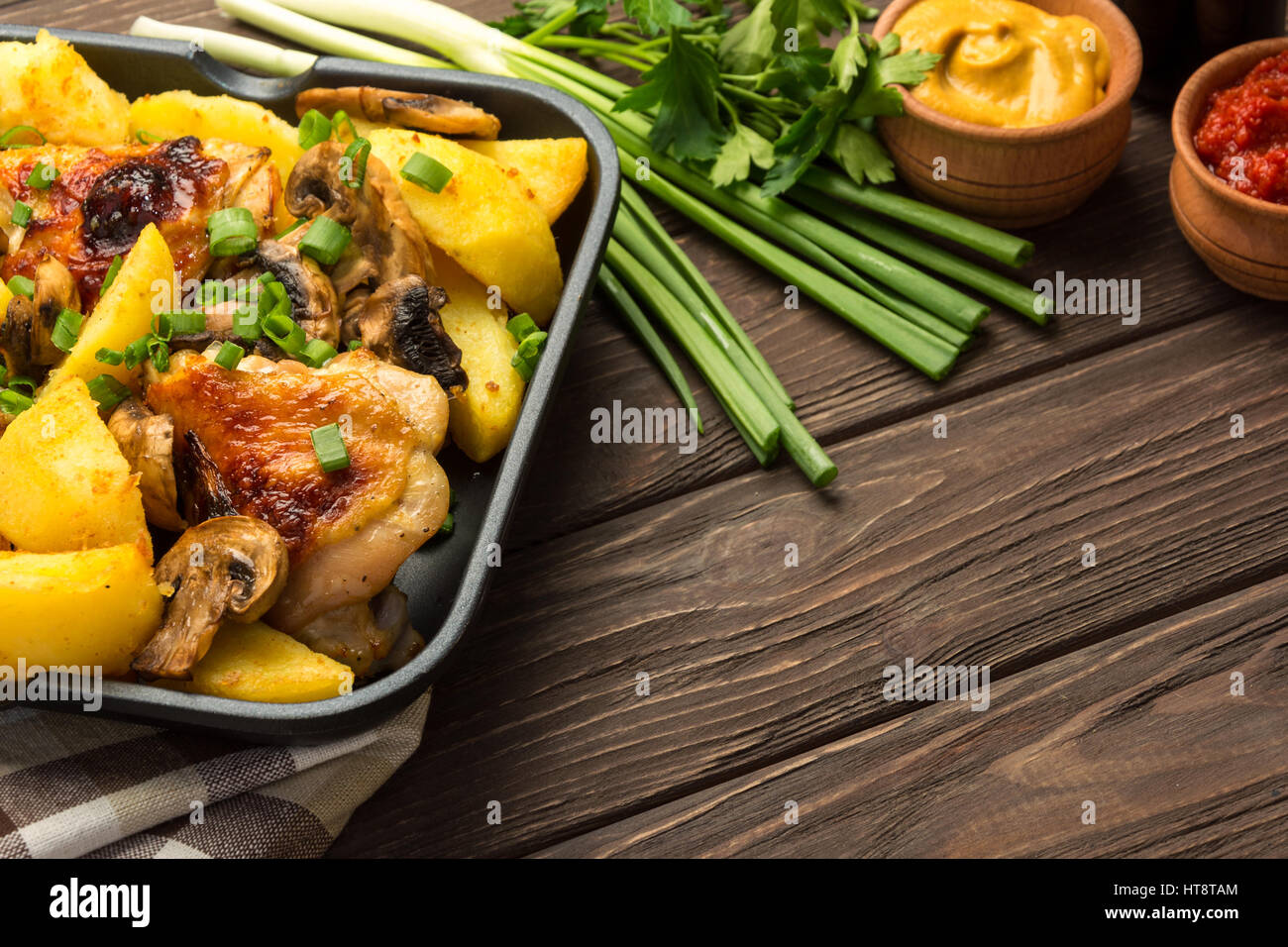 Dinner with baked chicken legs with olives spiced with aromatic herbs and potatoes with mushrooms on a rustic background.  Copy space. Stock Photo