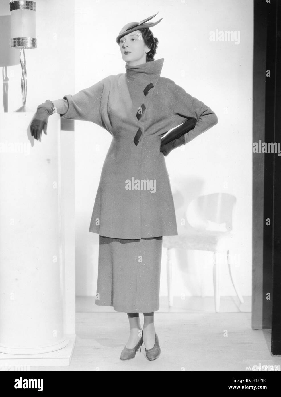 'Clothes have gone on the gold standard as is proven in this suit worn by Rosalind Russell in the new Metro-Goldwyn-Mayer production, 'Evelyn Prentice,' which co-stars Myrna Loy and William Powell. The suit is of beige woolen shot with metal threads. Brown suede thongs are used as fastenings. Accessories are in a matching shade of brown.' Stock Photo
