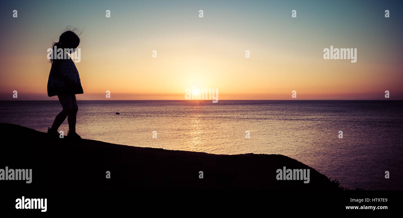 Little girl silhouette walking on hill at beautiful sunset over sea. Horizontal image with copy space Stock Photo