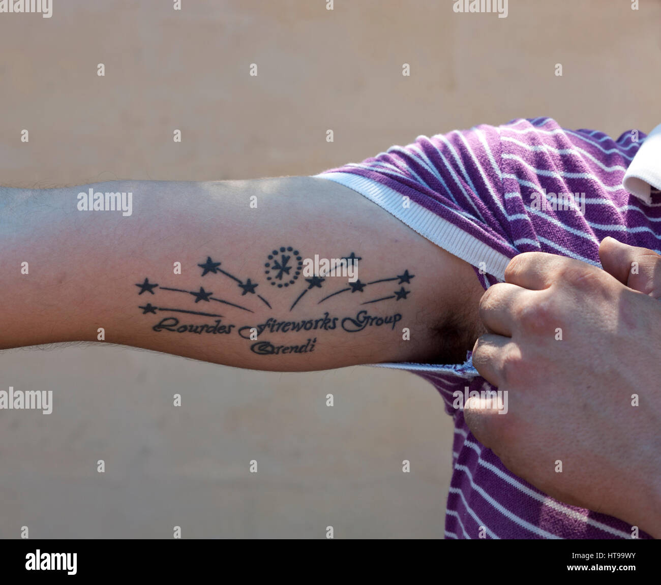 A Maltese pyrtechnician shows off the tattoo bearing the logo of the fireworks factory that he forms part of. Stock Photo