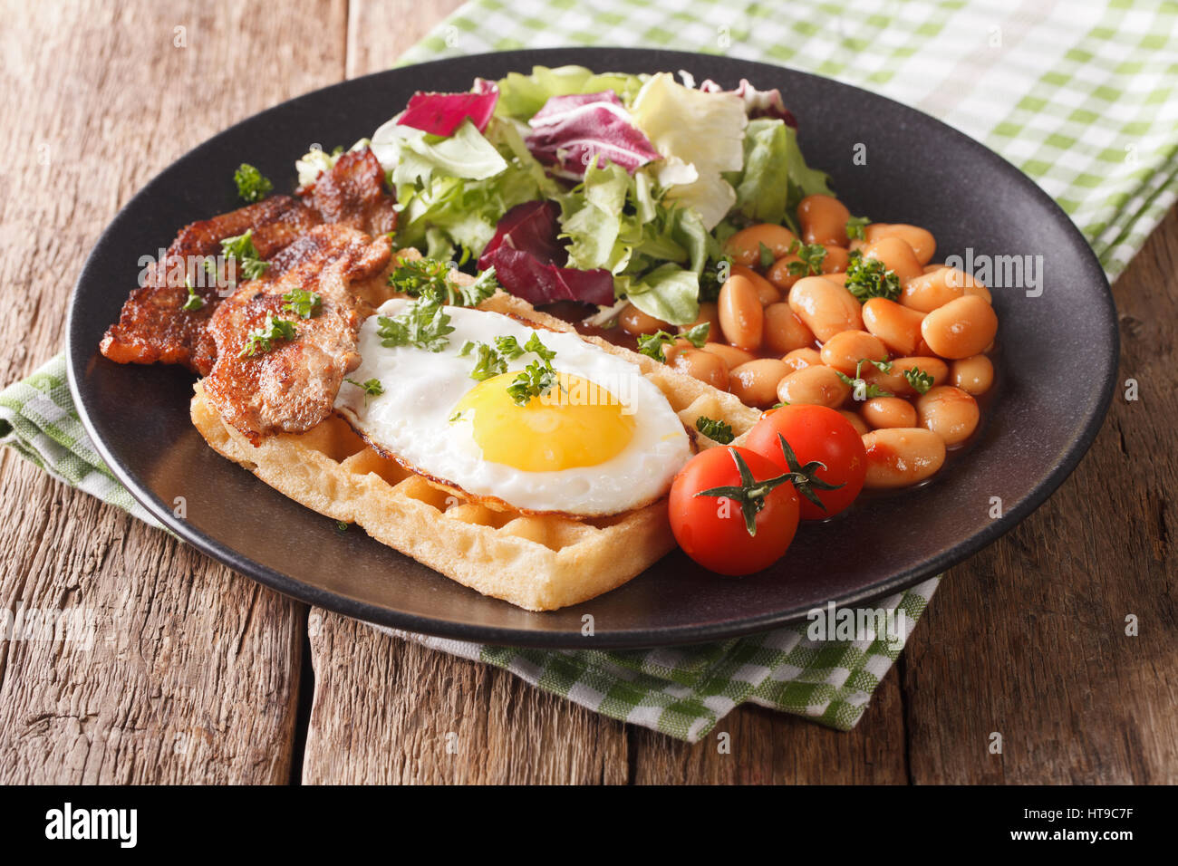 hearty breakfast with fried egg, waffles, bacon, mix salad and beans close-up on the table. horizontal Stock Photo