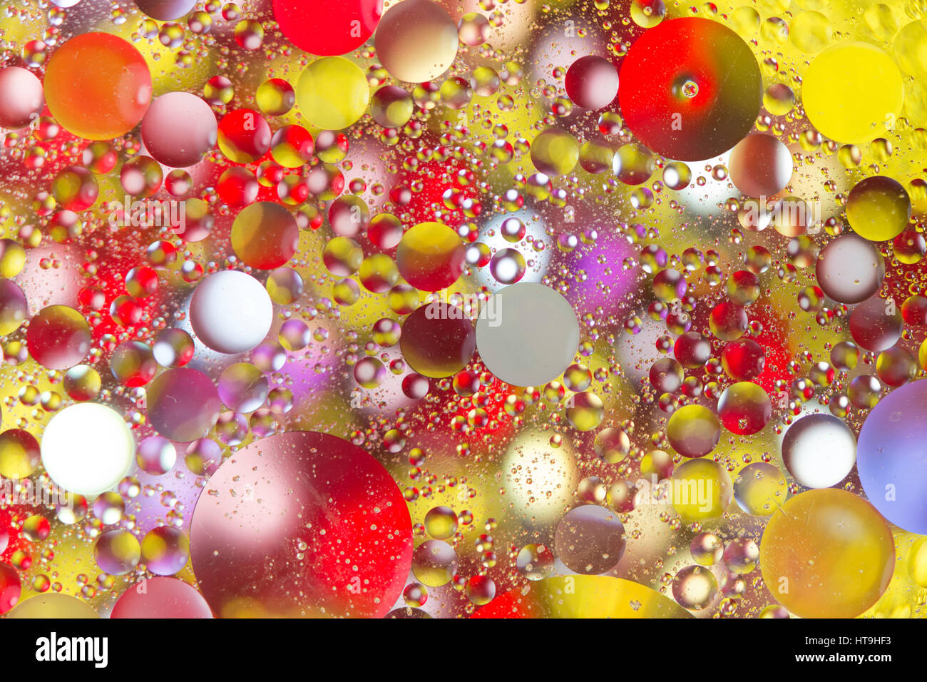 Backlit oil drops floating in water over colored beads Stock Photo