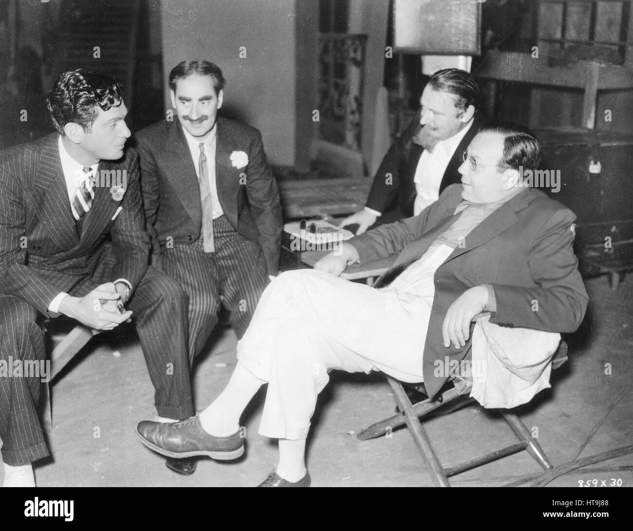 'Walter King, Groucho, Siegfried Rumann and Al Boasberg, gag man, enjoy a social chat while waiting for their next scene in 'A Night at the Opera,' the new Marx Brothers comedy, which Irving Thalberg is producing at the Metro-Goldwyn-Mayer studios. Sam Wood is directing the new picture.' Stock Photo