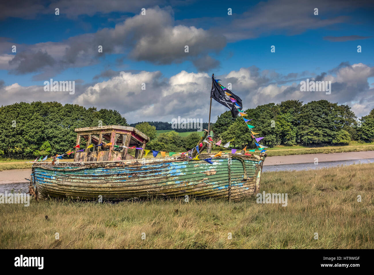 An old boat by the dee in Kirkcudbright decorated with bunting and a scull and crossbones pirate flag. Taken in Dumfries and Galloway, Scotland, UK. Stock Photo