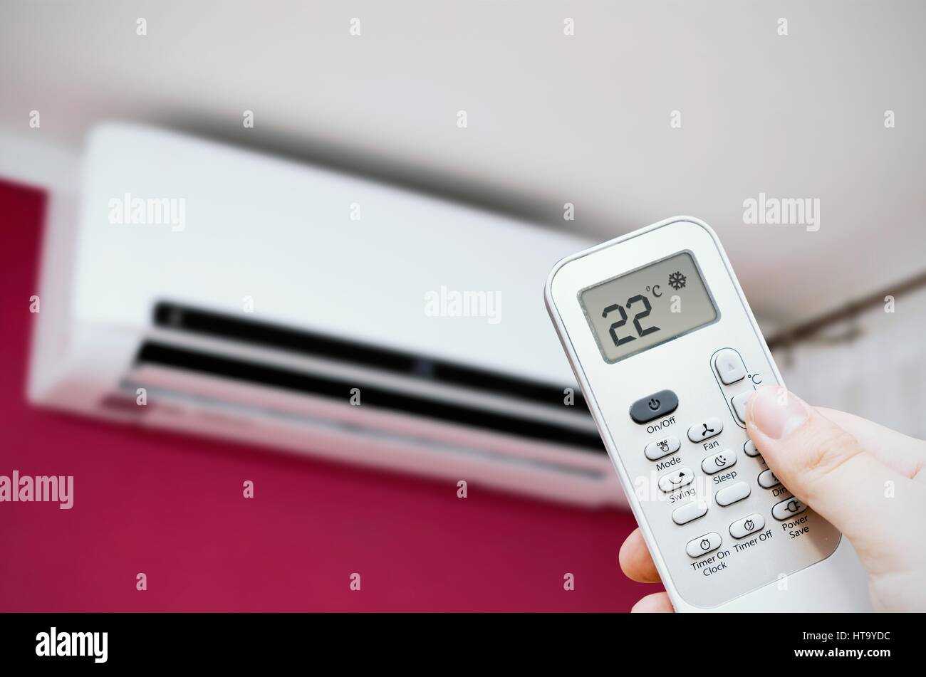 Air conditioner split on the wall. Hand holding remote control Stock Photo