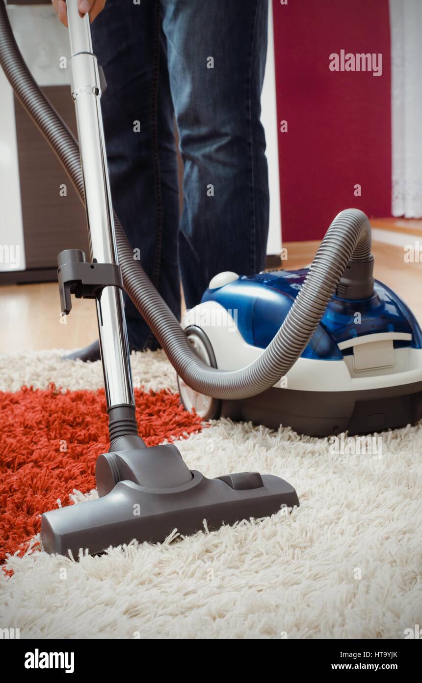 Man vacuums shaggy carpet in the apartment. Modern blue vacuum cleaner Stock Photo