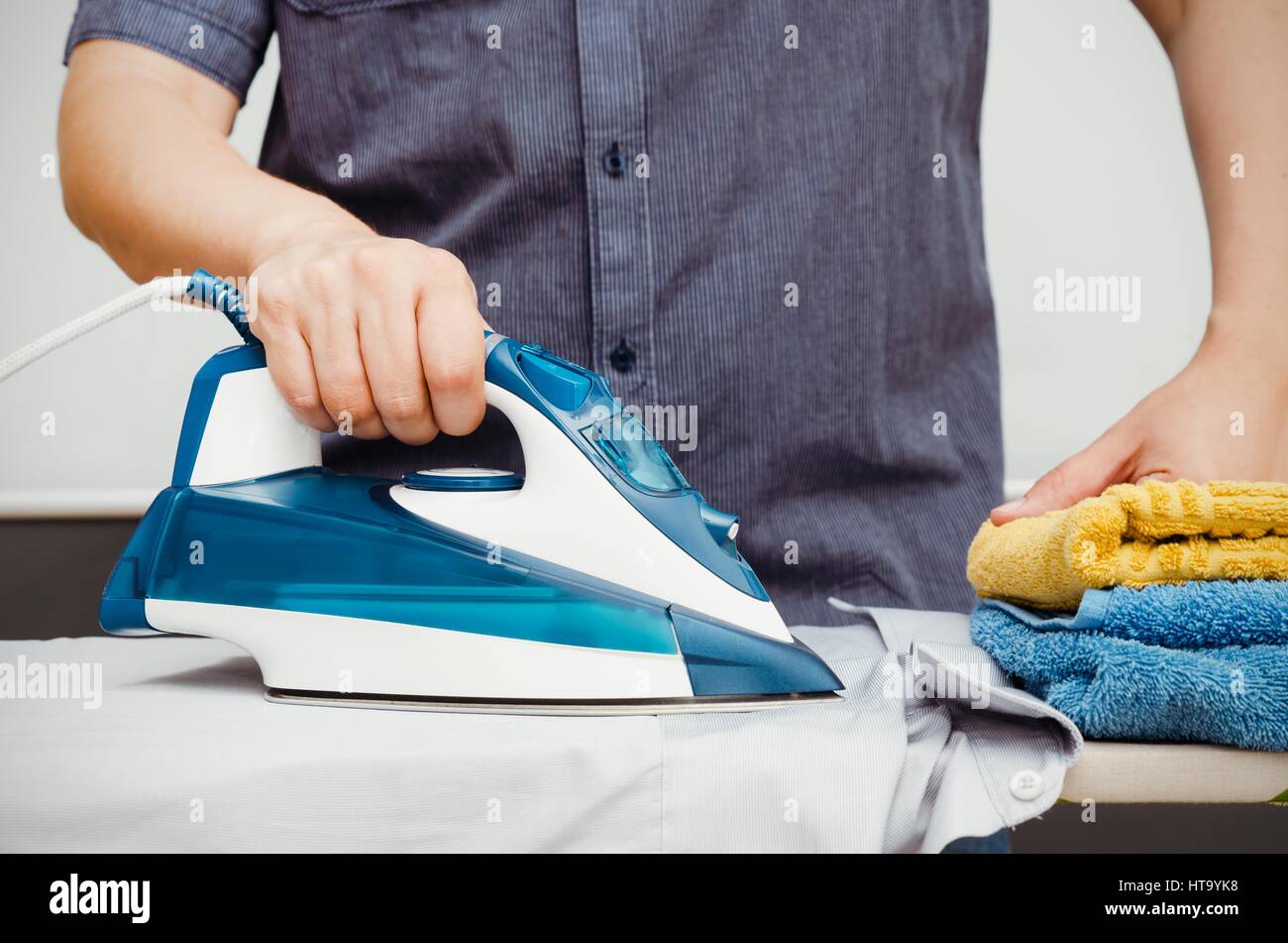 Man irons clothes on ironing board with steaming blue iron Stock Photo