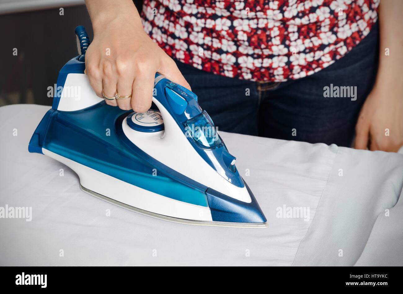 Woman irons clothes on ironing board with blue steaming iron Stock