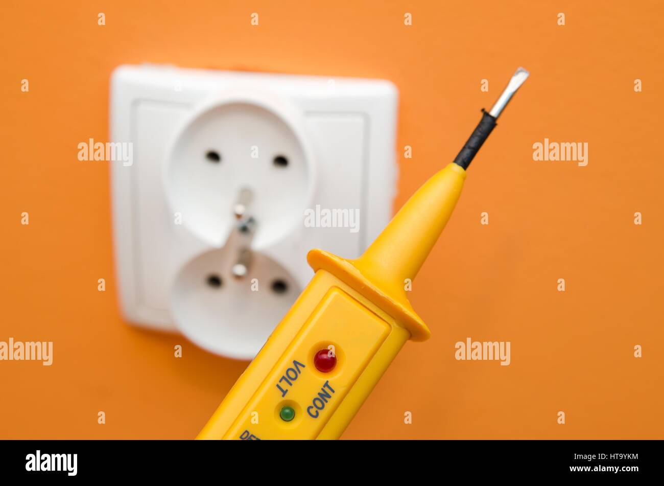 Electricity current meter, turn-screw near to the socket on orange wall. Stock Photo